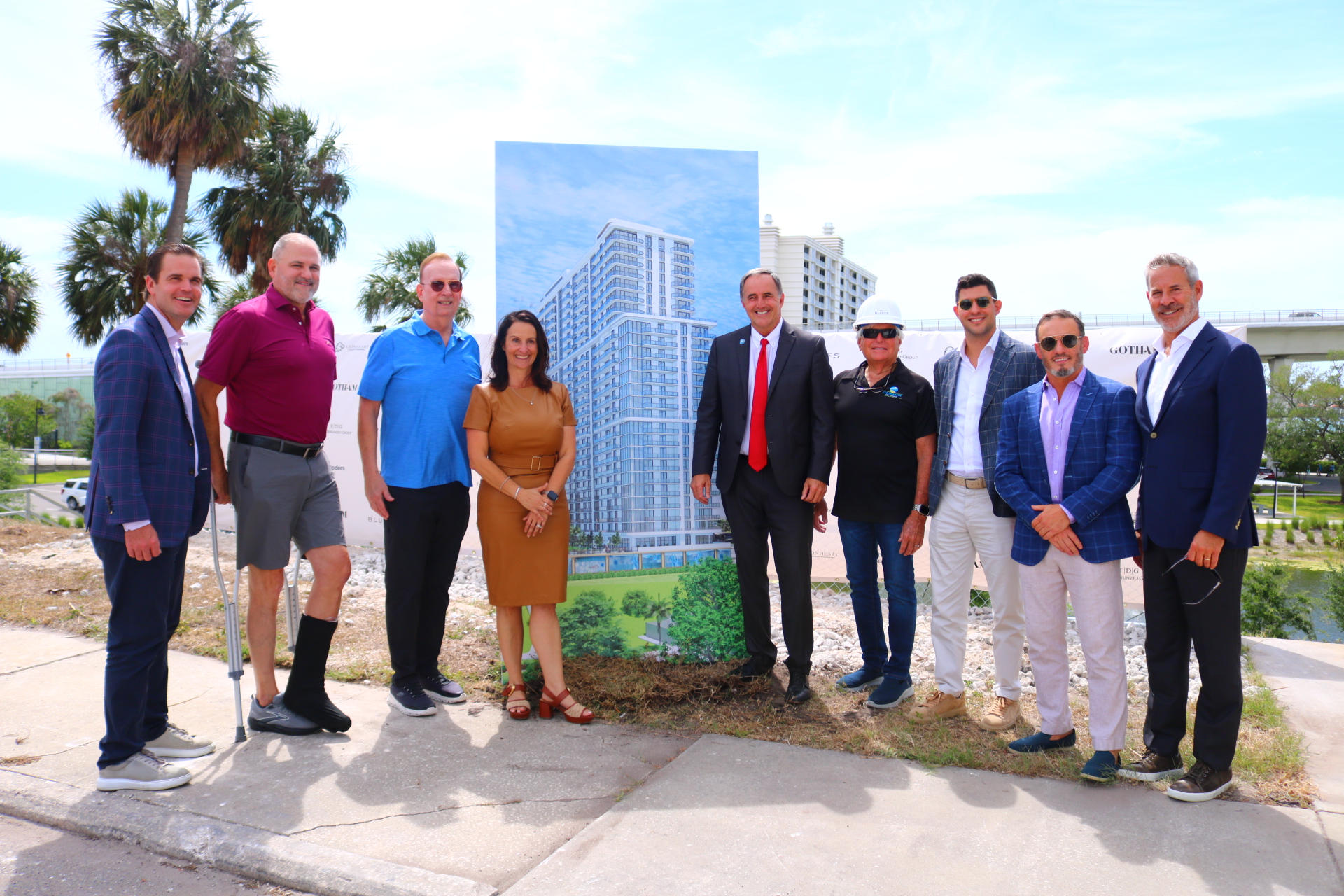 8 men and one female in front of large picture of the apartment complex