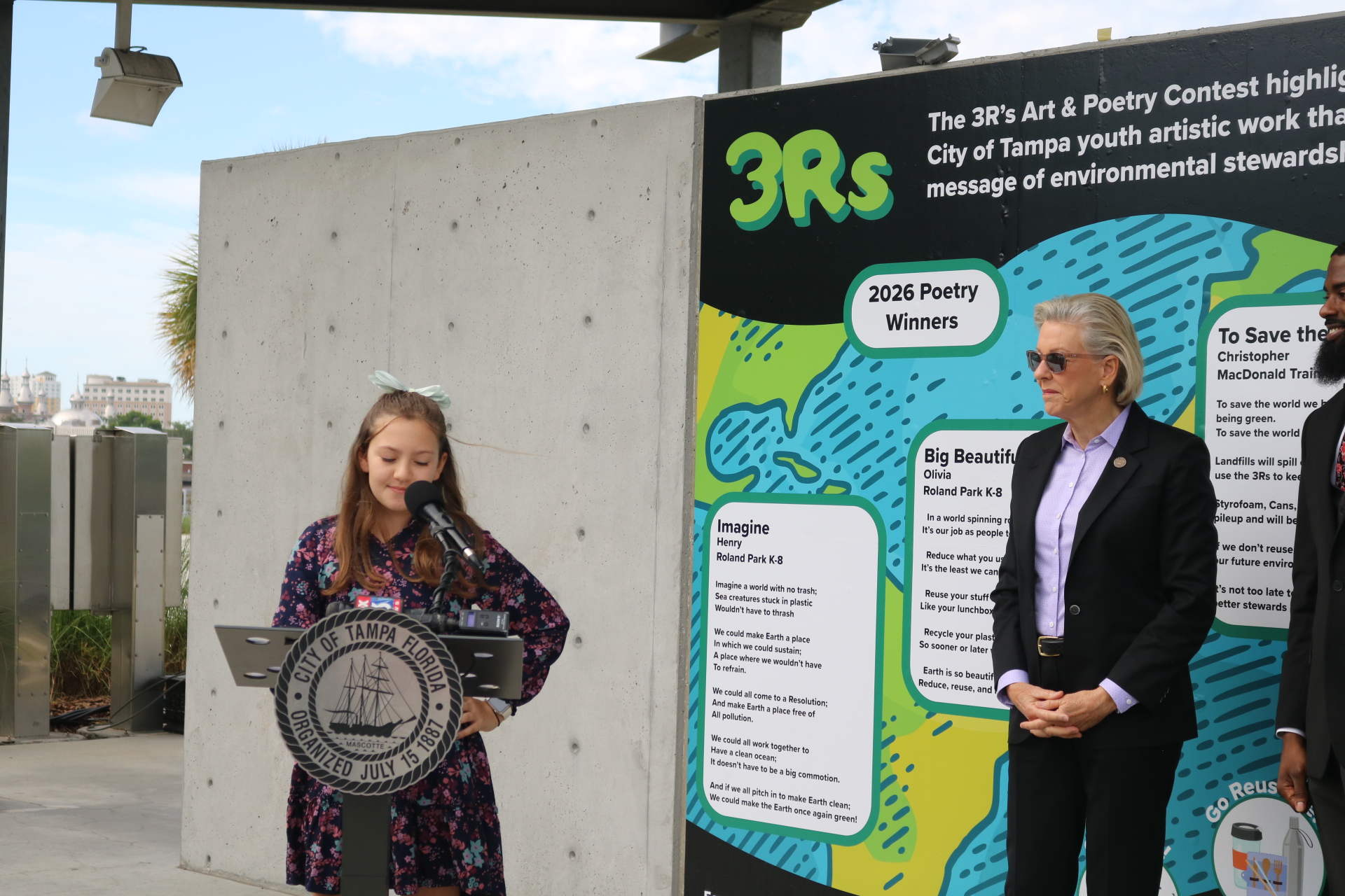 A young girl speaking at a podium with Mayor Jane Castor on her right.