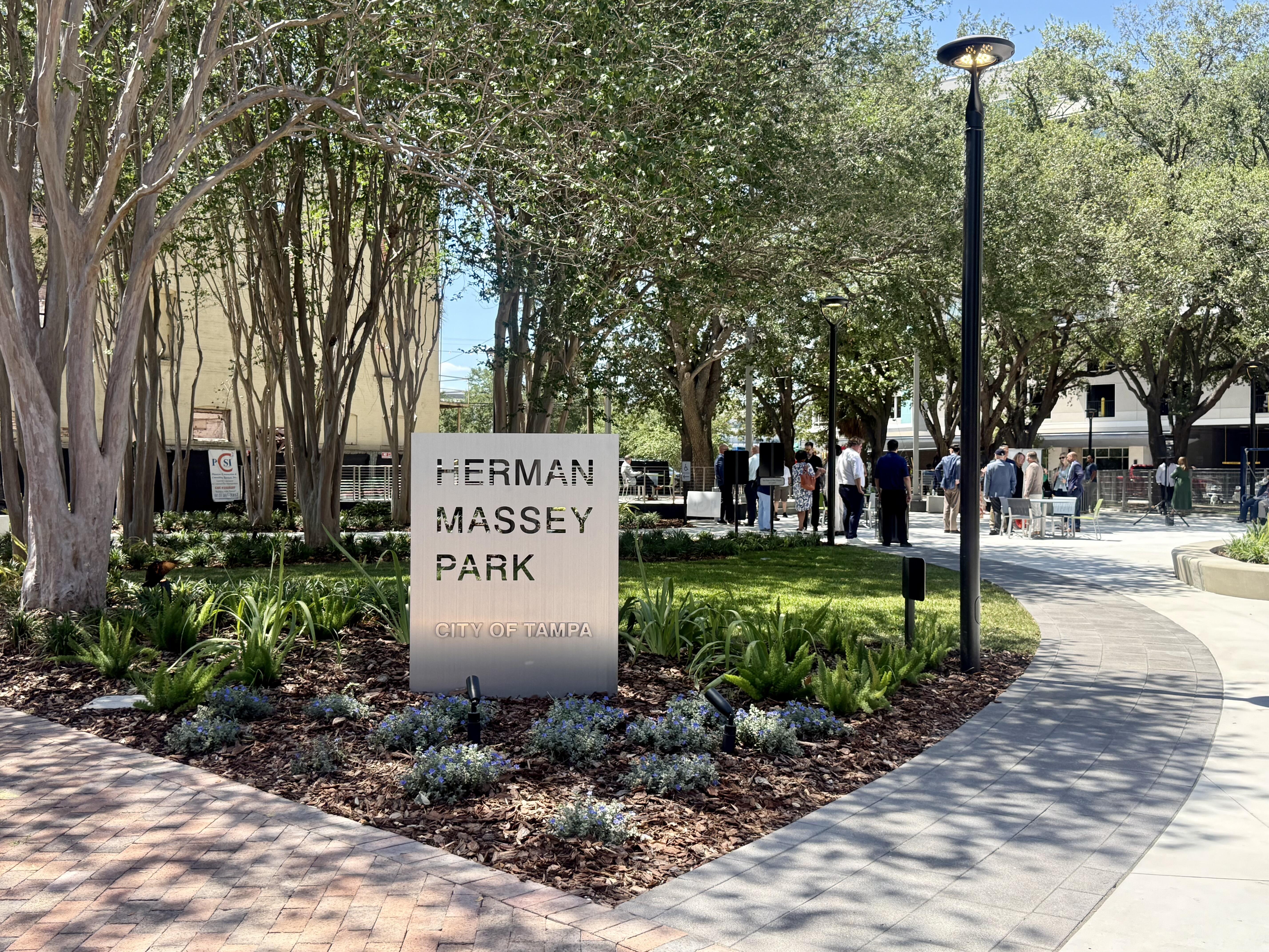 Metal sign that reads Herman Massey Park in a park next to oak trees.