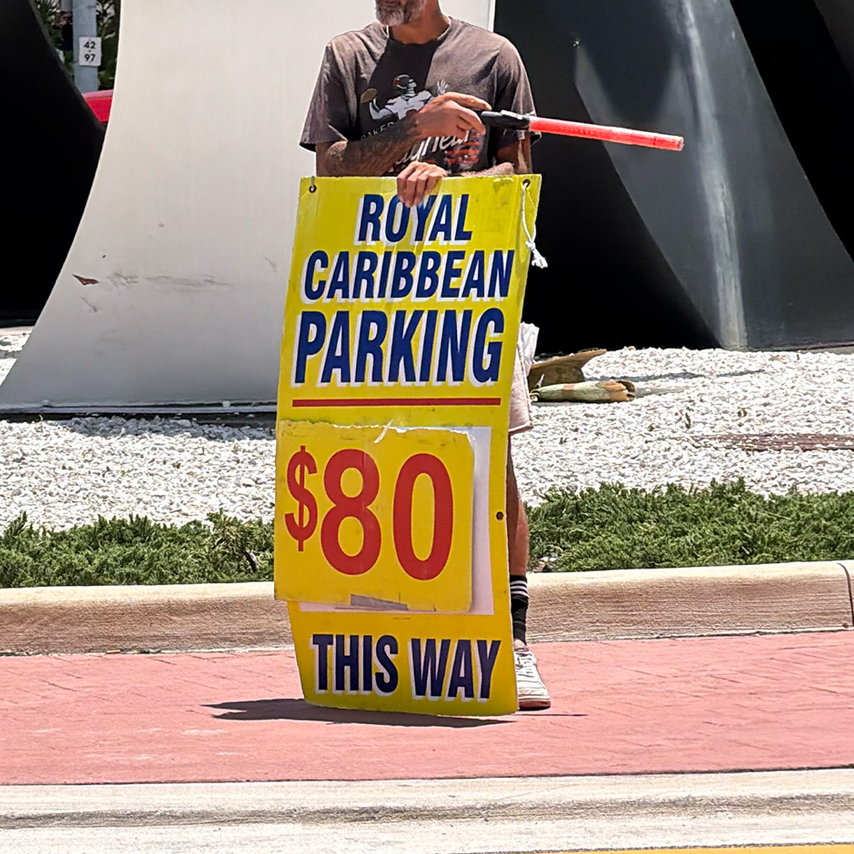 Parking operator holding a yellow sign that says 'Royal Caribbean Parking $10 This Way'