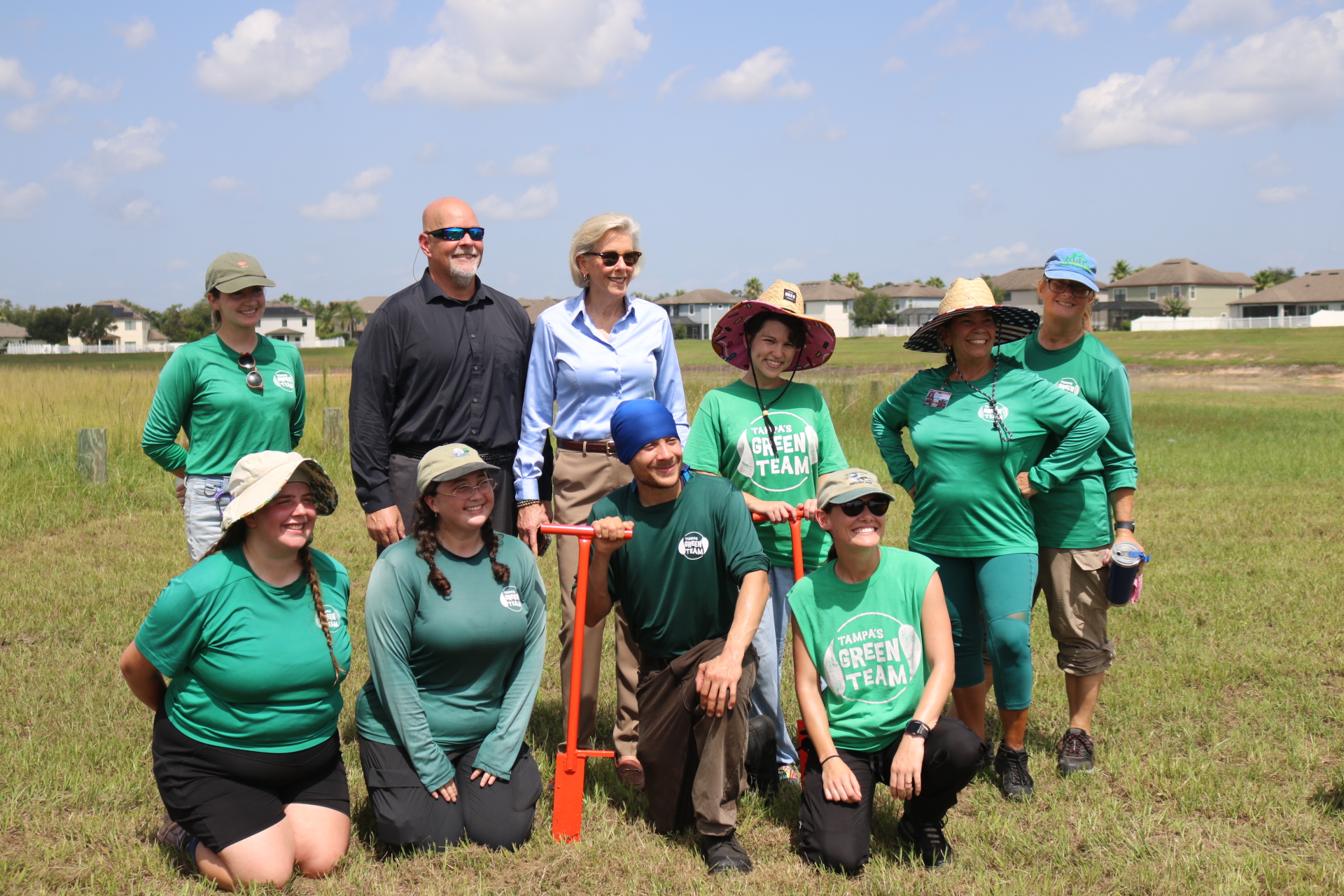People in green shirts with an orange shovel smiling for picture
