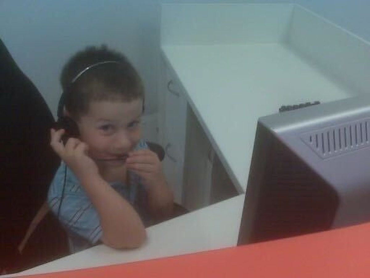 A young Ryan Shatzkamer wearing a call center headset and smiling at a desk next to a computer monitor