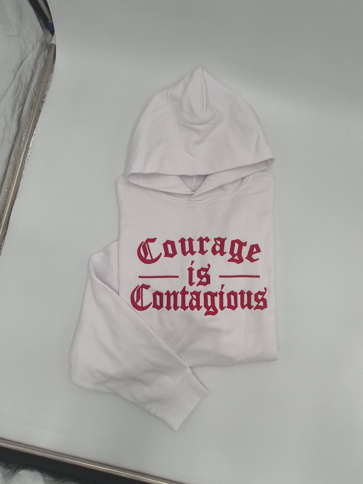 A person wearing a Frazier Brand shirt with the words Courage is Contagious printed on the front.