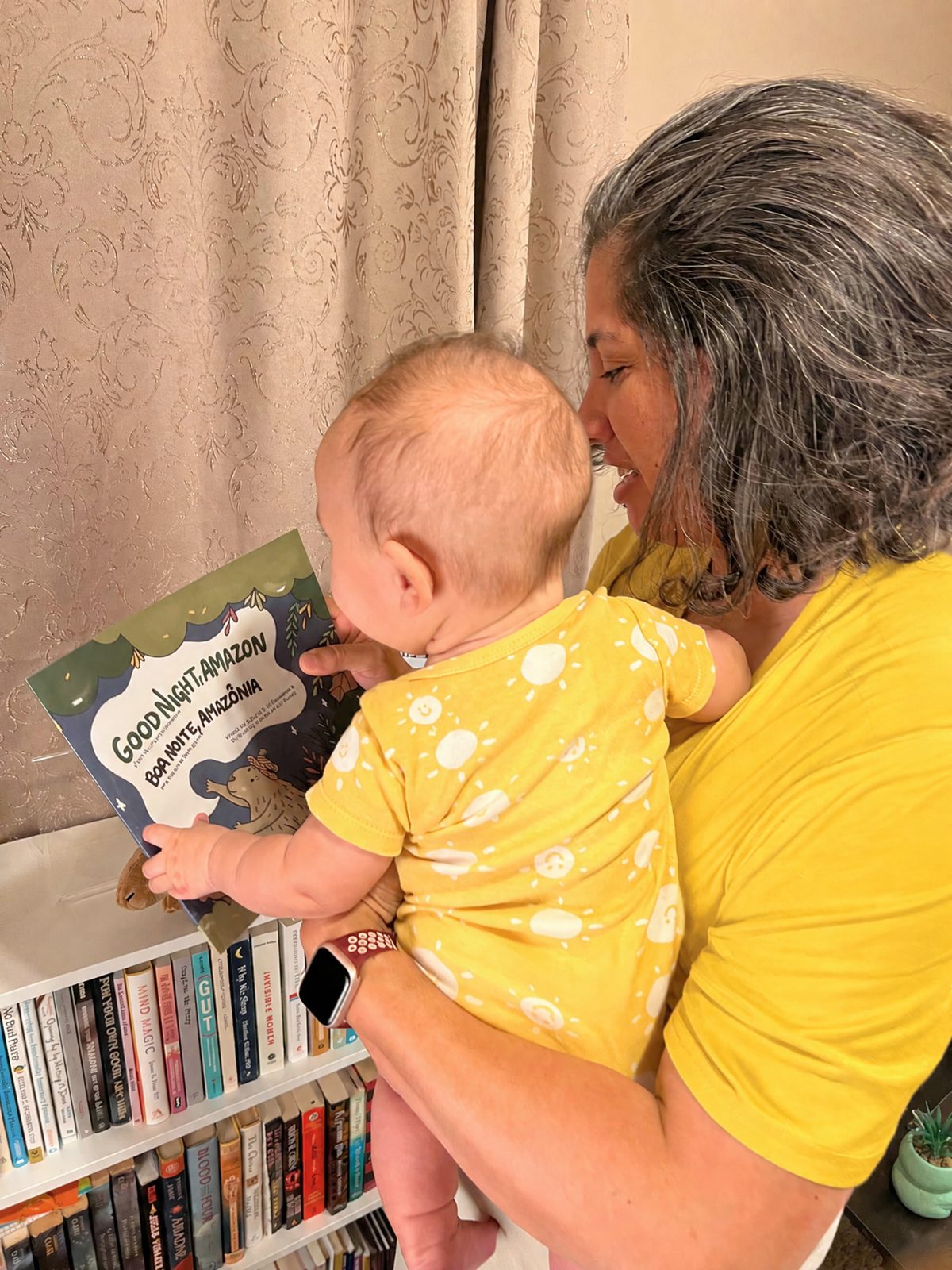 A child reading a Portuguese-English picture book with a caregiver, colorful illustrations visible on the open pages.